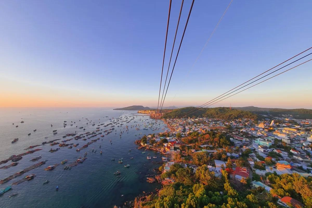 A city is seen from a cable car, with a beautiful sunset casting a warm glow over the landscape.