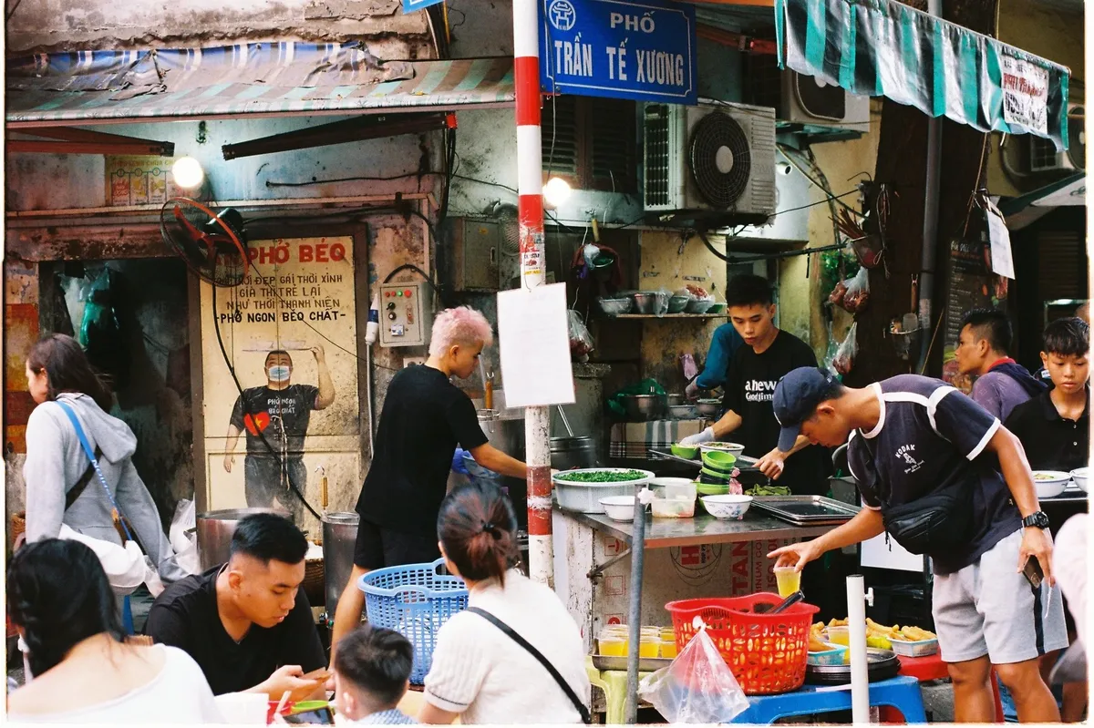A group of people are sitting at a table in front of a food stand.