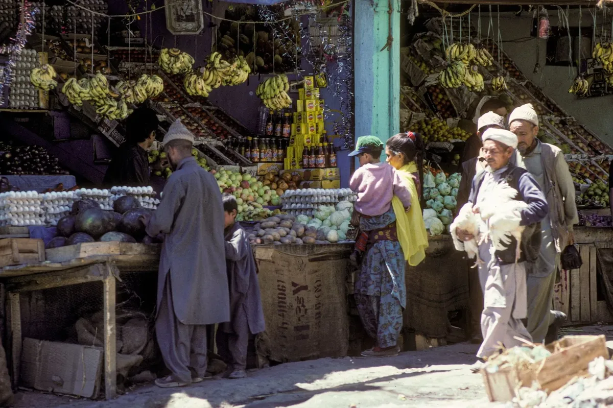A group of people are shopping at a market with a variety of fruits and vegetables.