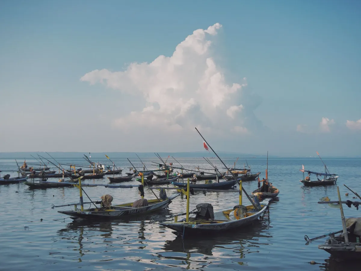 A group of boats are floating in the water, with a cloudy sky above.