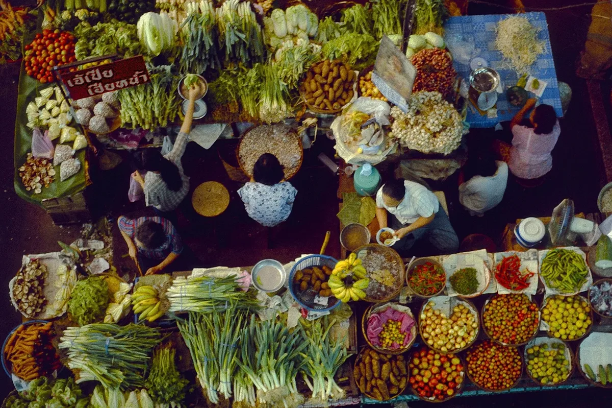 A market scene with people shopping for vegetables and fruits.