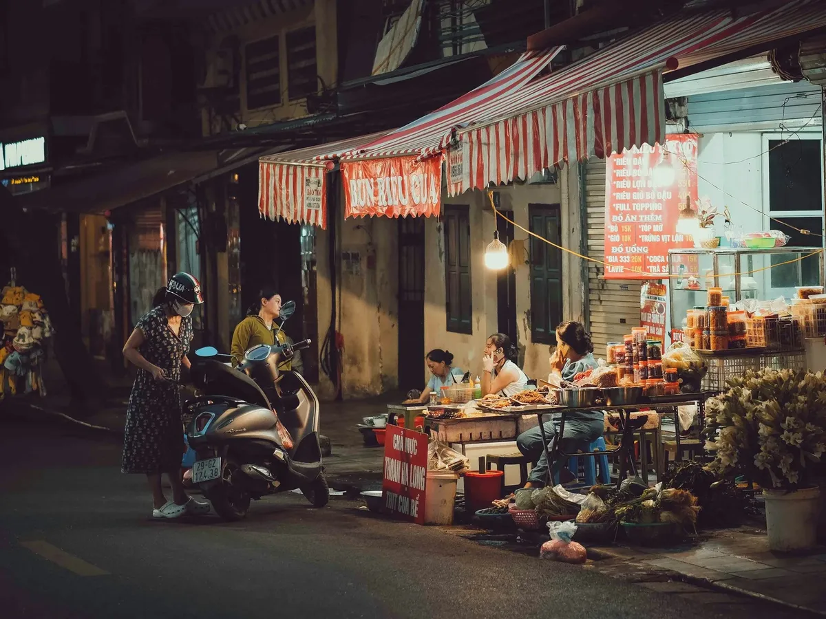 A group of people sit at a table outside a store at night.