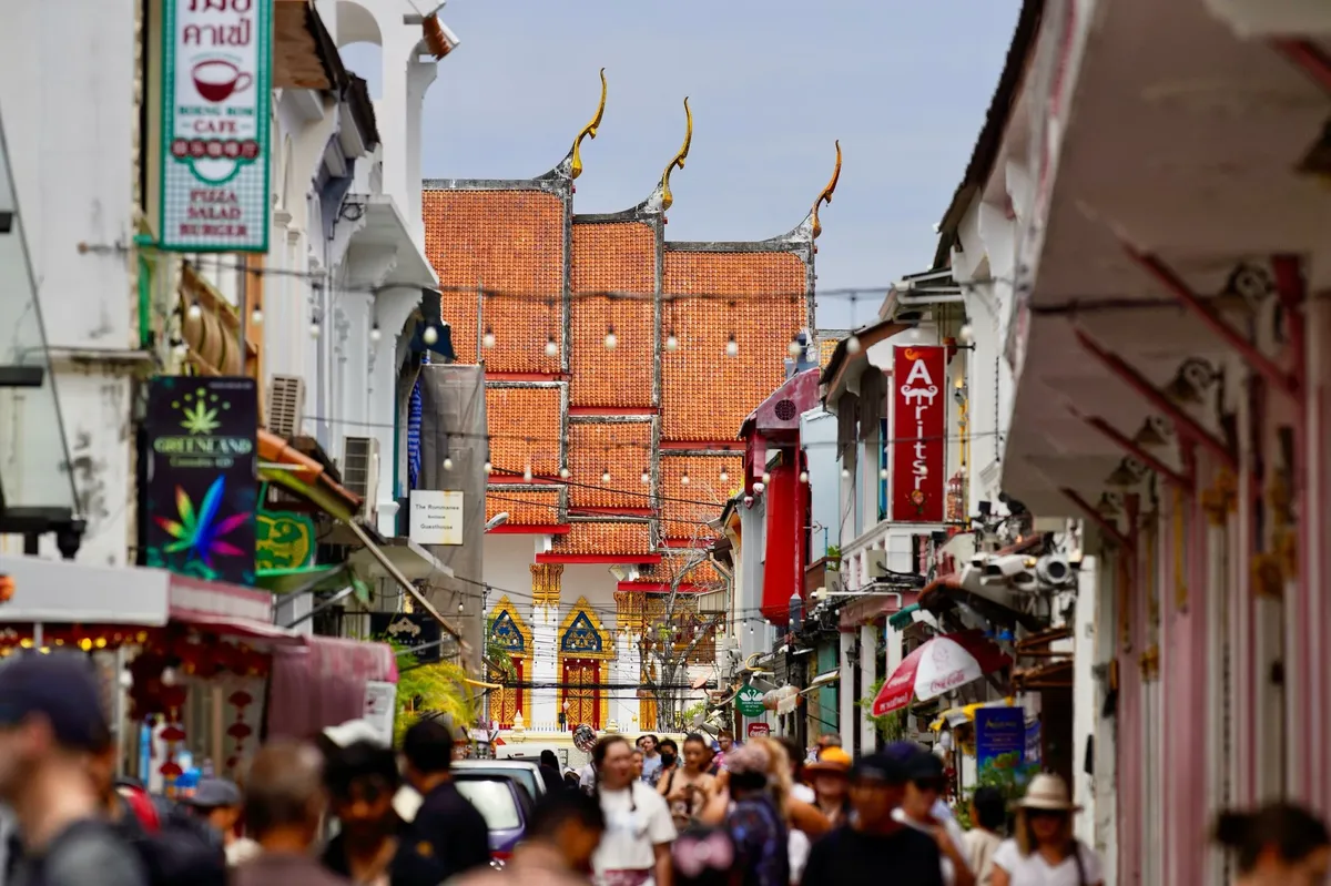 A busy street in a foreign country with people walking and a red building in the background.