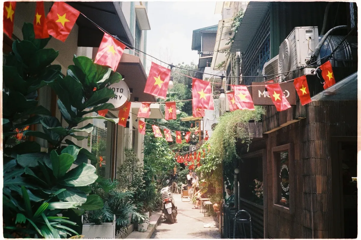 A street in Vietnam with red, white, and blue flags hanging from the buildings and a motorcycle parked on the side of the road.