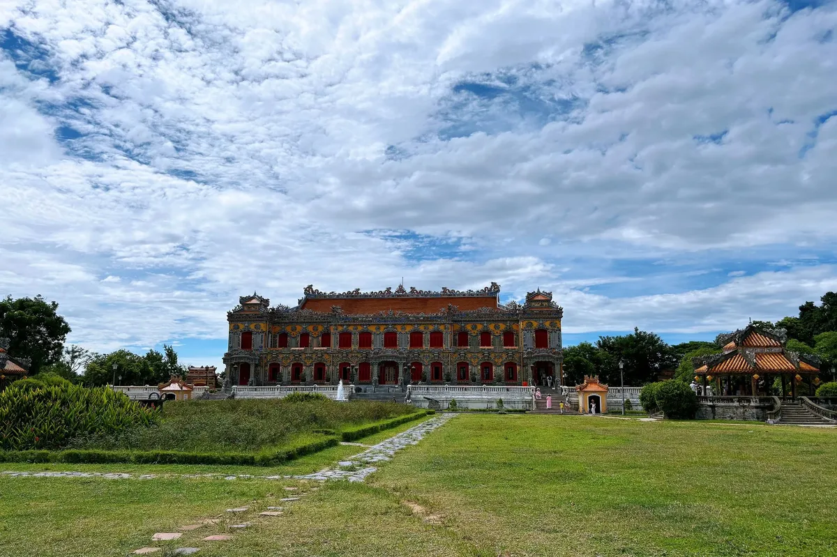 A large building with a red roof and white walls sits in a grassy field.