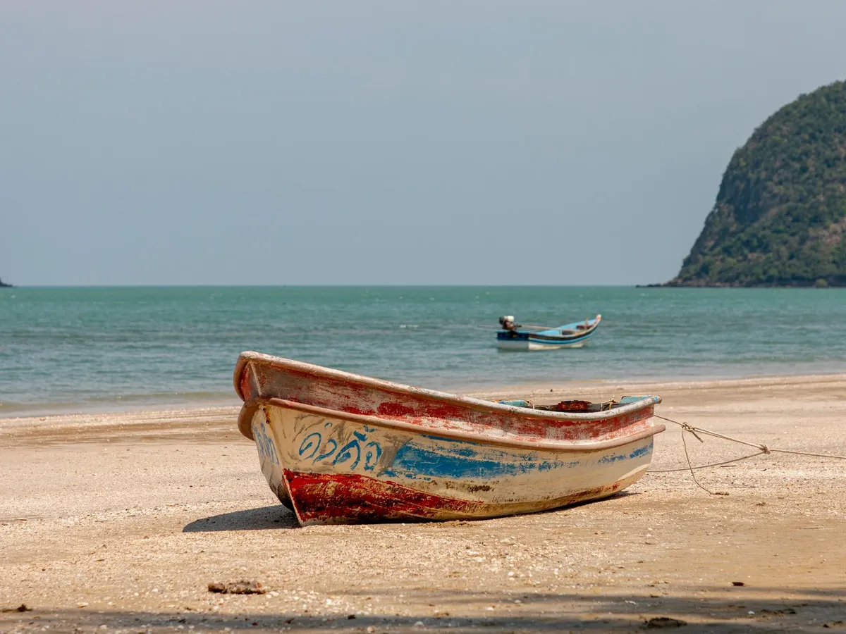 A boat is sitting on the beach in front of a mountain.