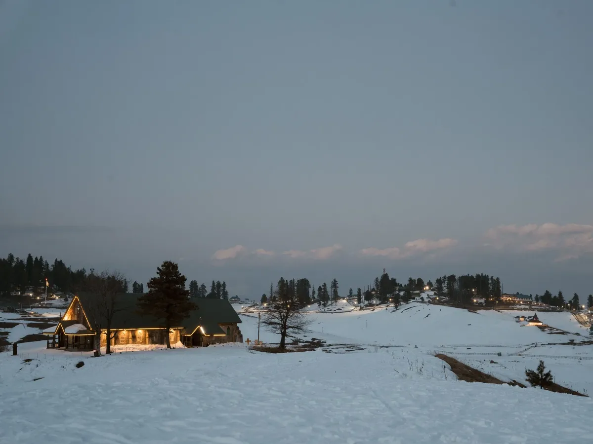 A snowy field with a house in the background and a tree in the foreground.