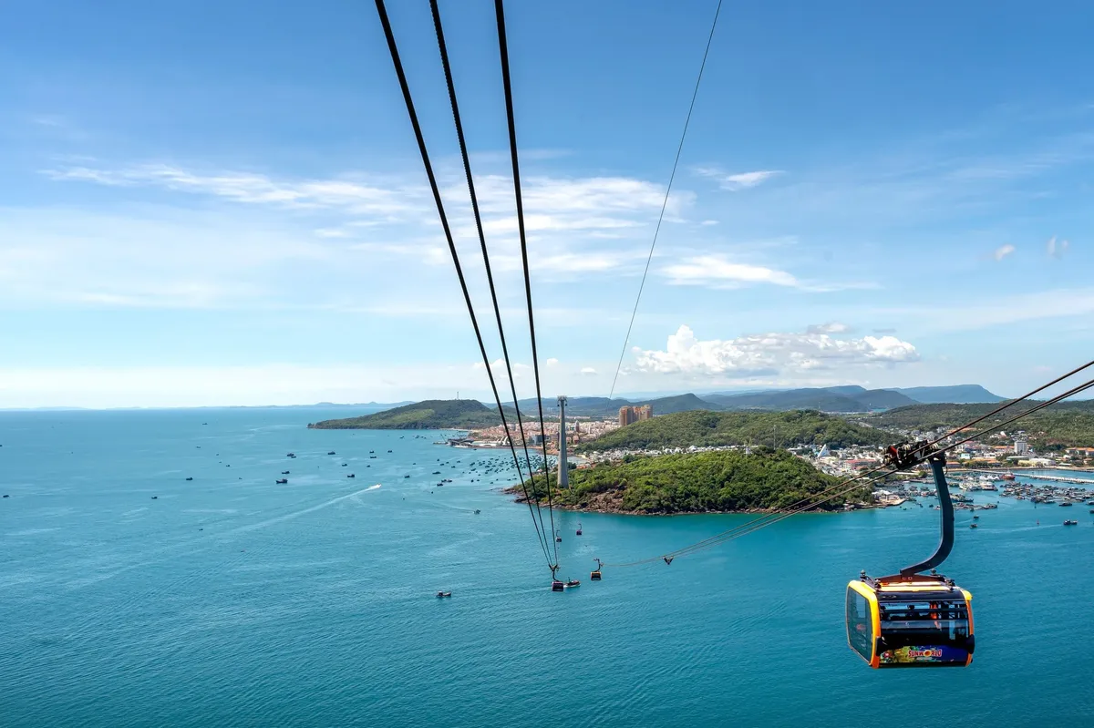 A cable car is flying over a beautiful island with a city in the background.