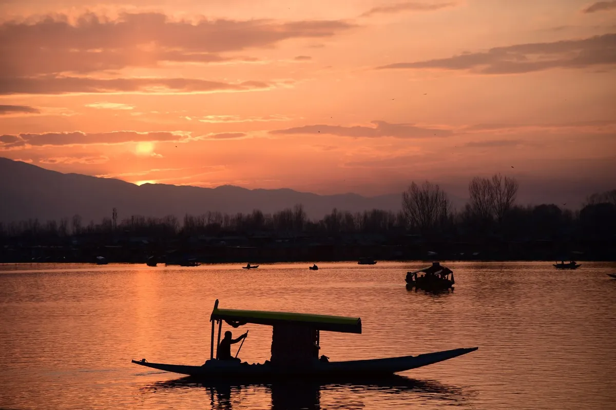 A boat with a yellow canopy is on a lake at sunset.
