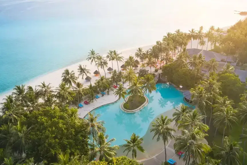 A resort pool between palm trees and the beach on an island in Ari Atoll