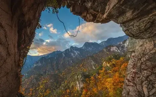 Autumn-coloured mountains seen through a rocky cave opening