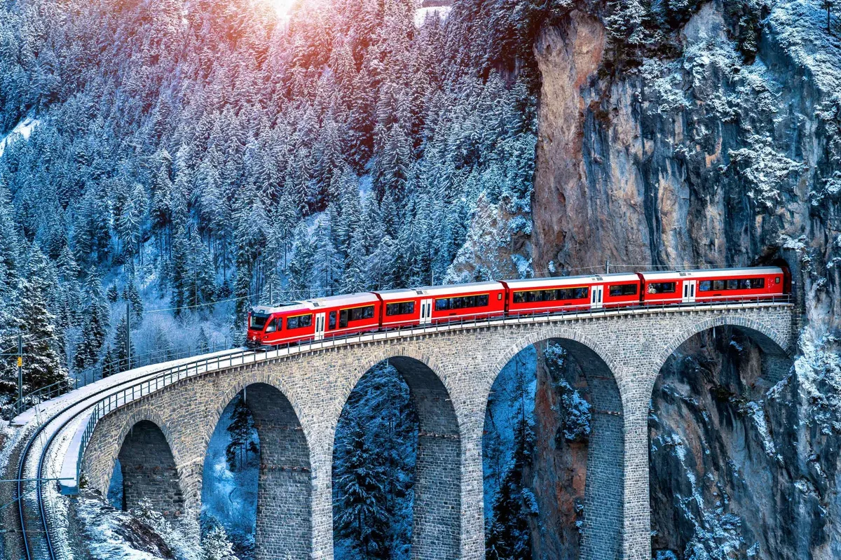 A red train crossing the stone Landwasser Viaduct in snowy forest