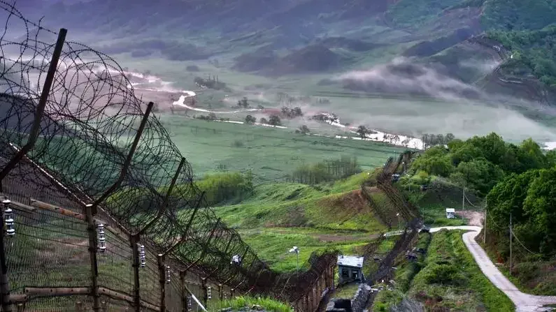 Barbed-wire fences of the DMZ running down green hills in the mist