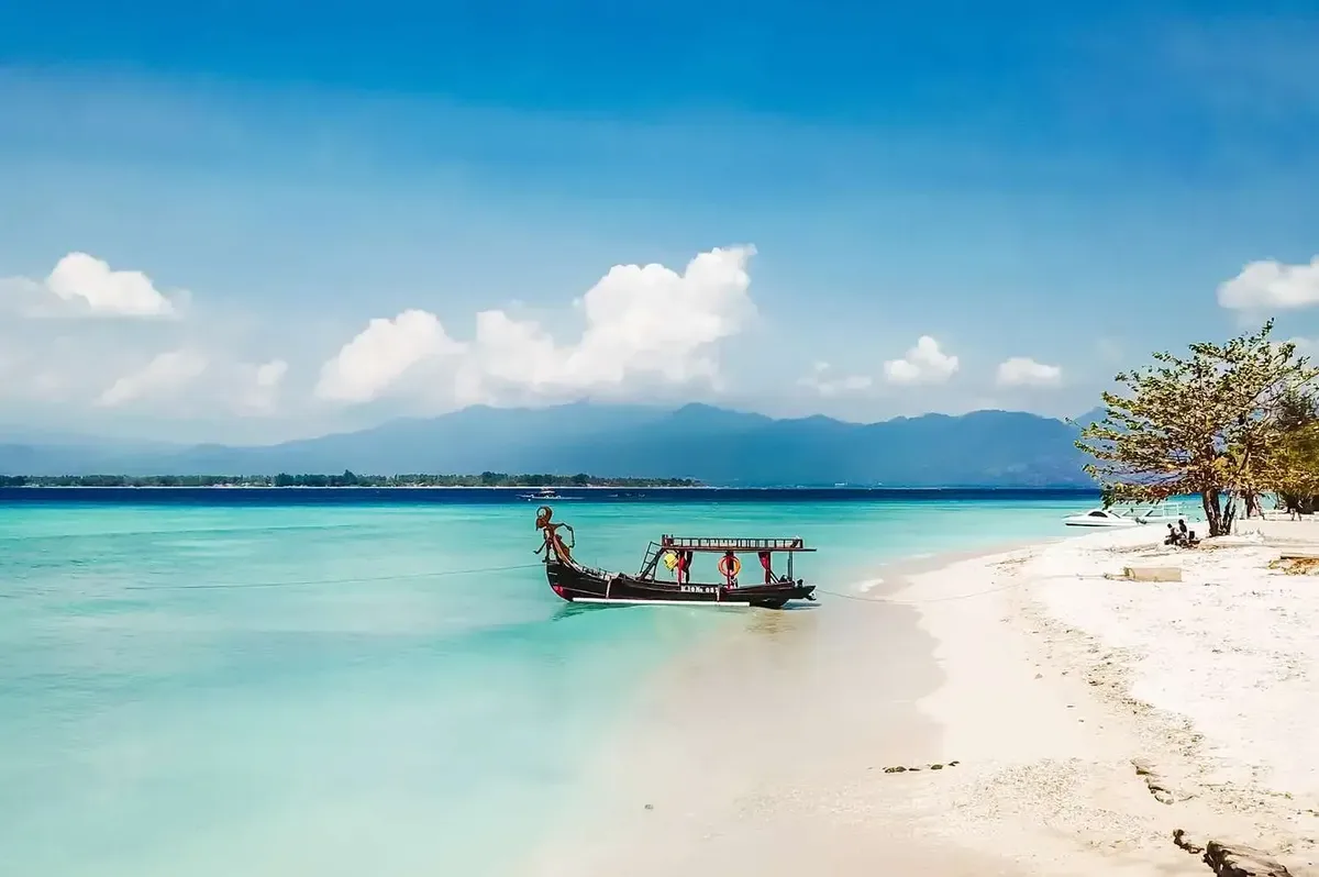 A wooden boat on clear water off a white beach in the Gili Islands