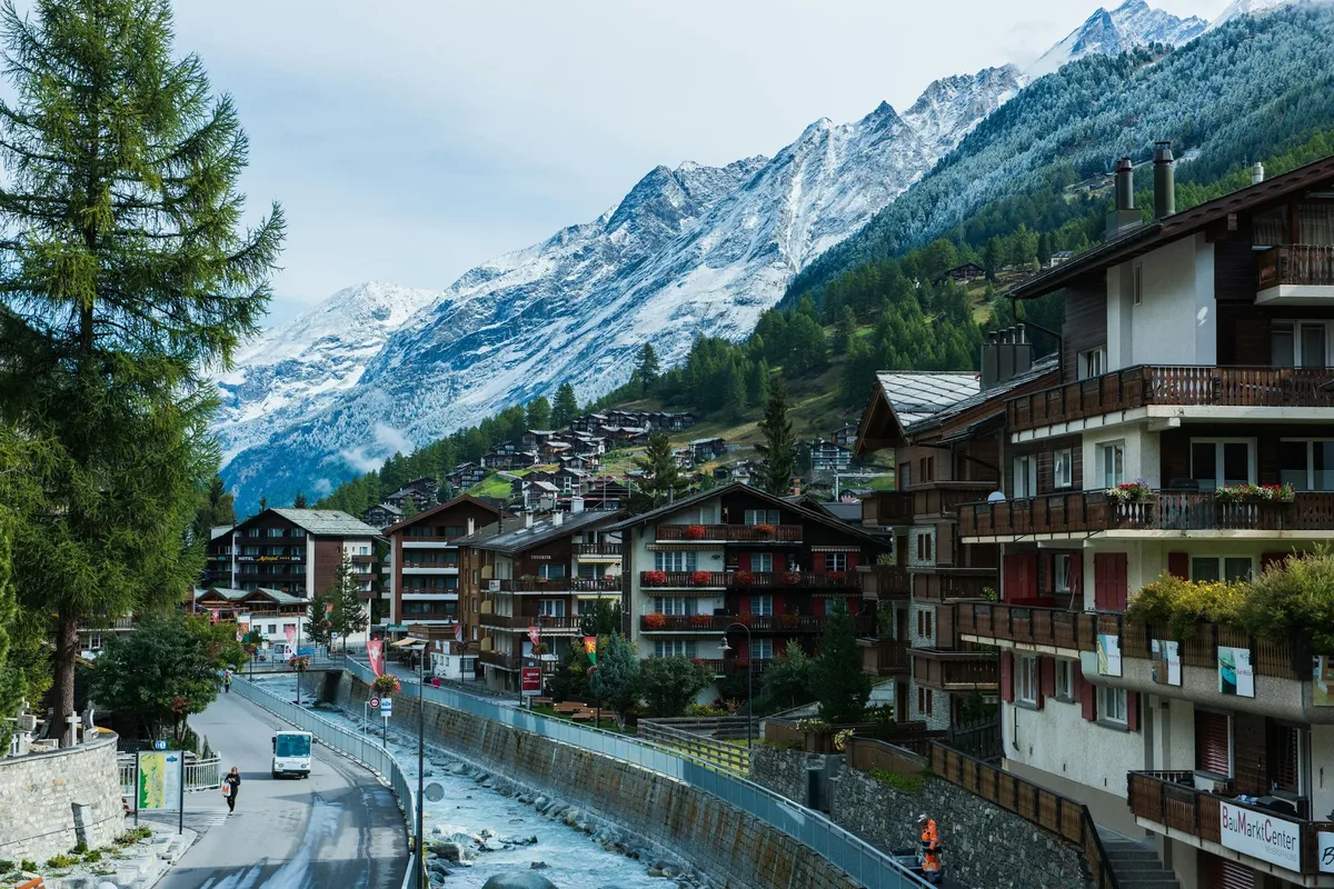 Wooden chalets along a village street with snowy peaks behind