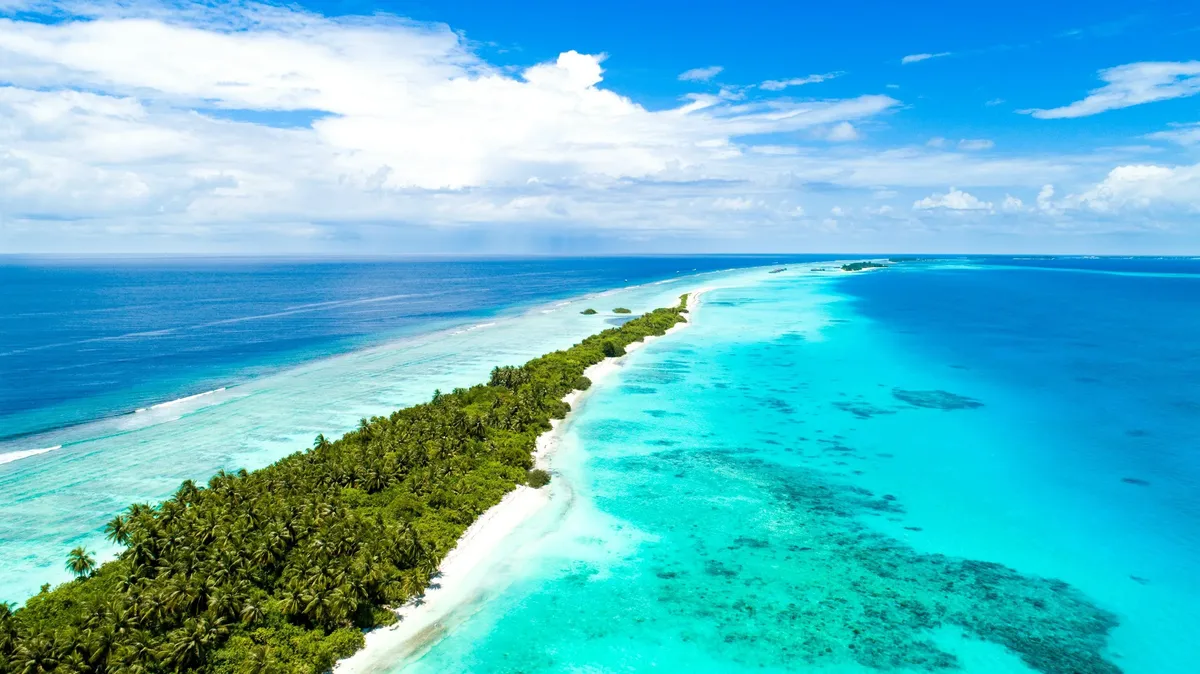 A thin island of palms between a turquoise lagoon and the open ocean in the Maldives