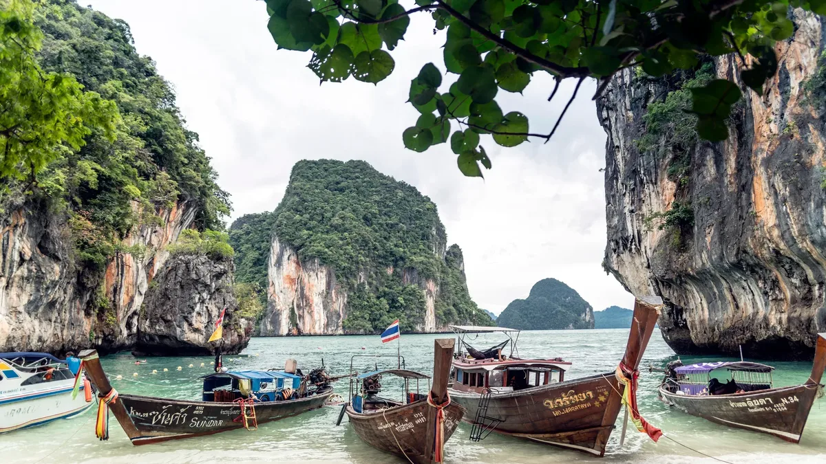 Longtail boats on a beach below limestone cliffs in southern Thailand