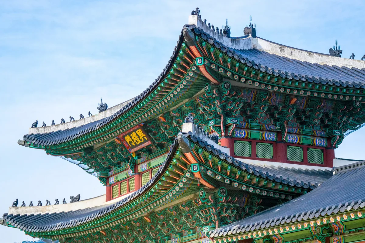 The painted eaves of a palace gate in Seoul against a blue sky