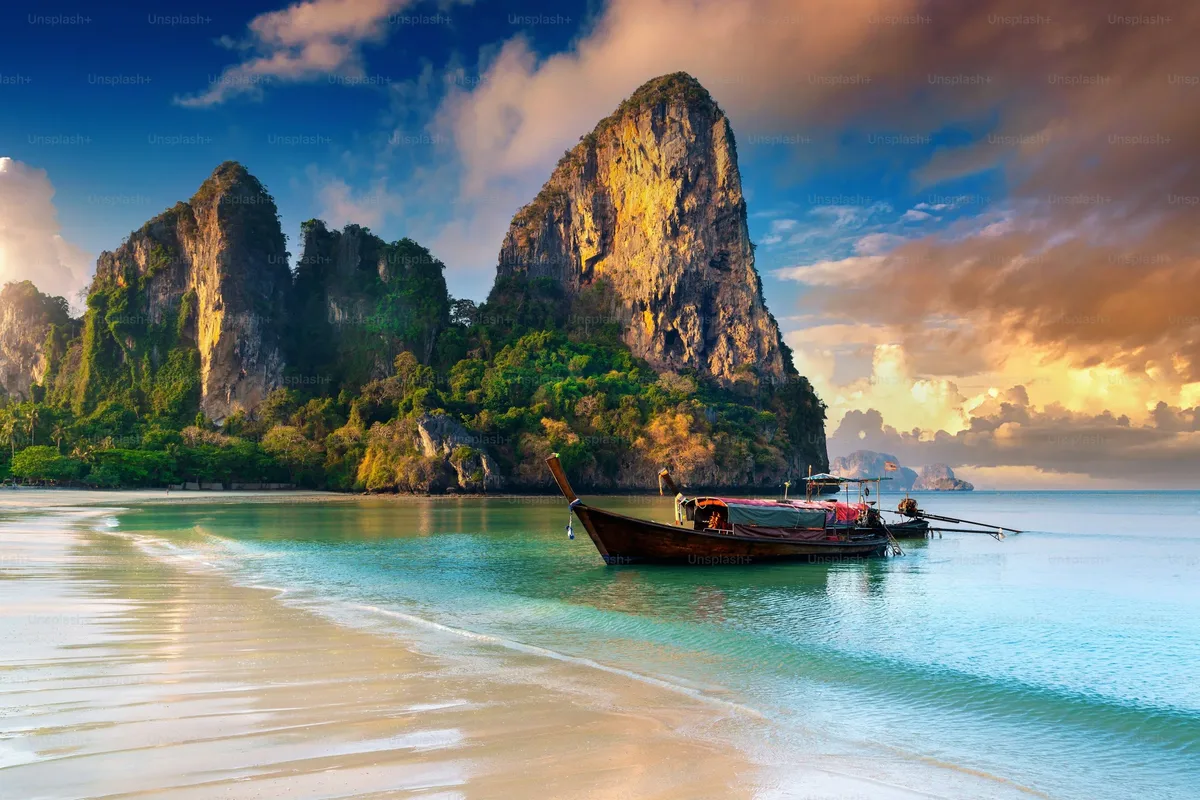 A long-tail boat off a white-sand beach with limestone islands behind