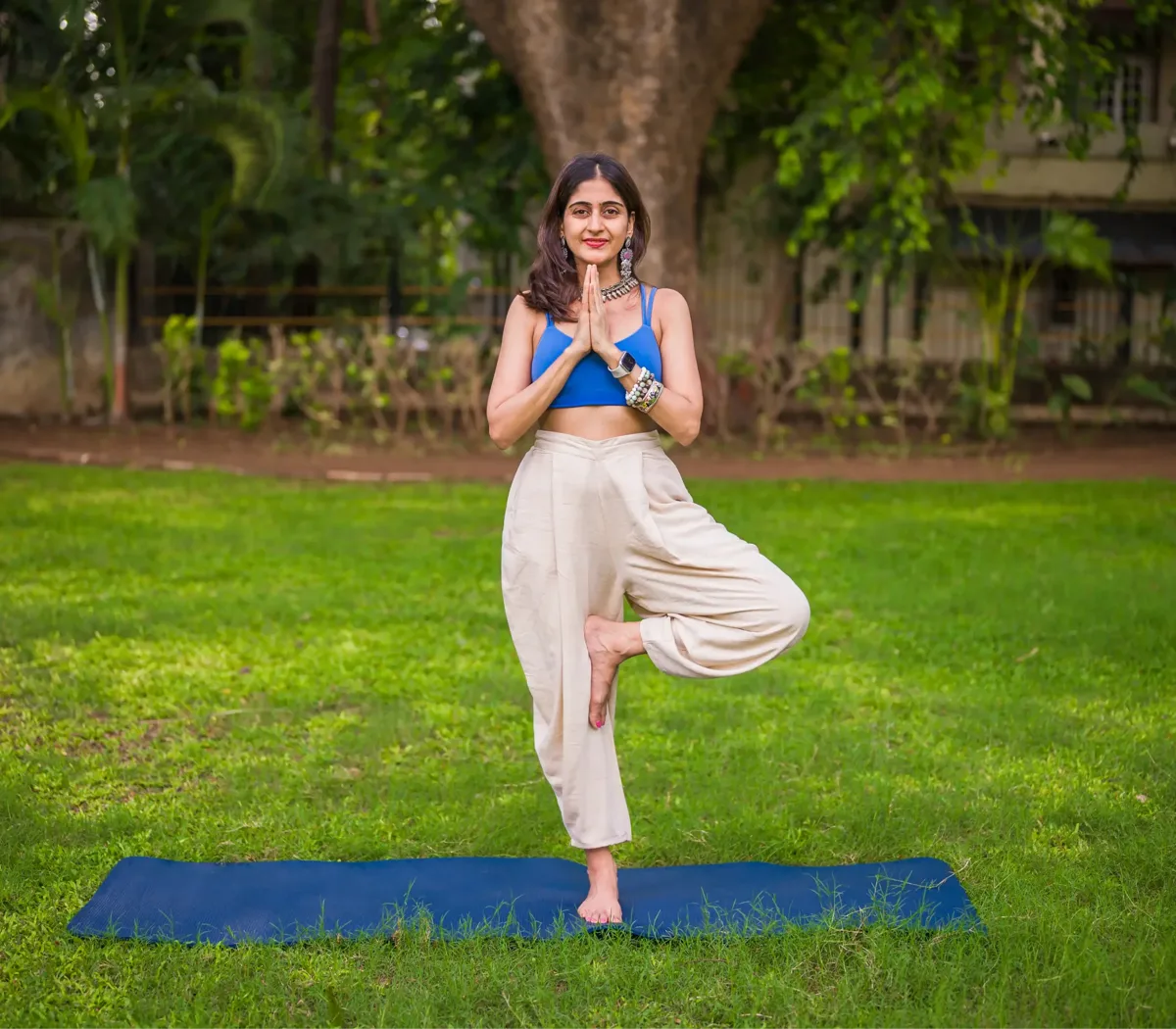 A woman in a blue shirt and white pants is doing yoga in a grassy field.