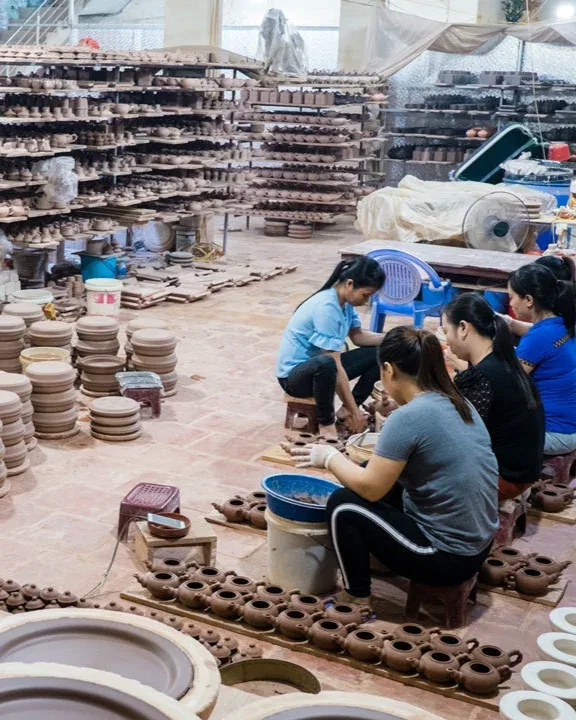 A group of women sit on the floor in a room filled with clay pots.