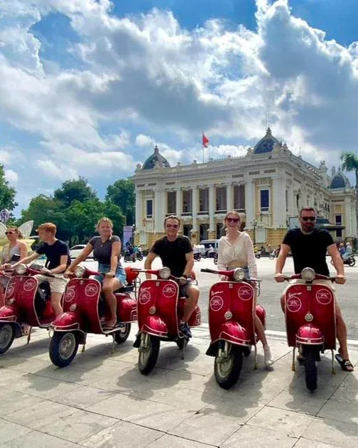 A group of people riding red scooters in front of a large white building.